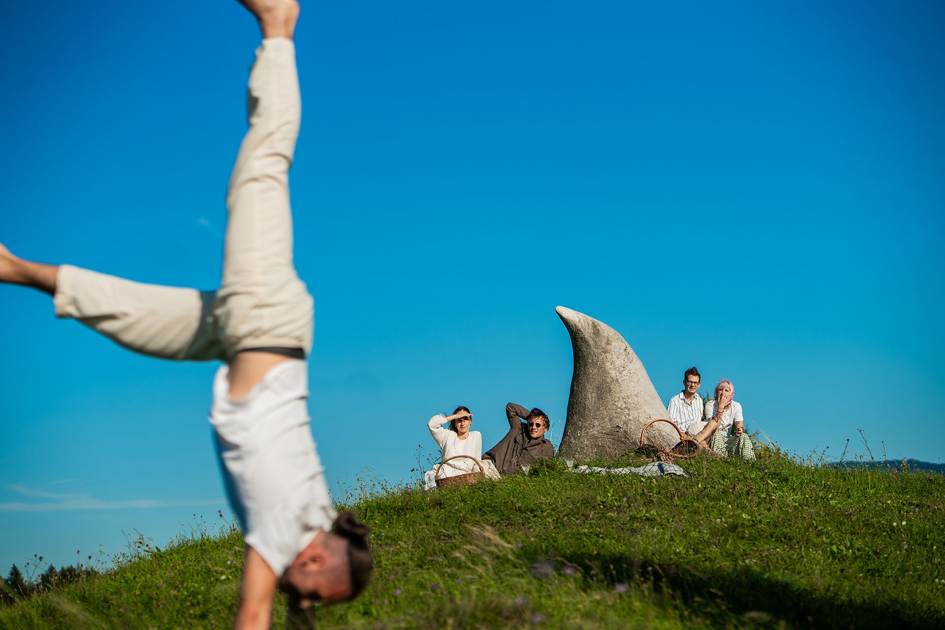 Friends resting on a sunlit hilltop beside a boulder under a deep blue sky.